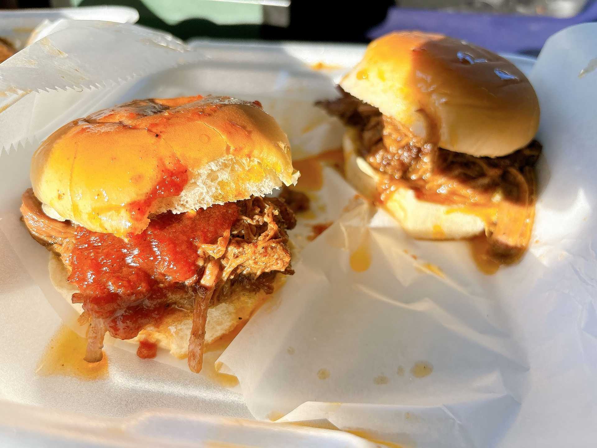 Pulled pork sliders with rich sauce on soft buns, presented on crumpled parchment paper.