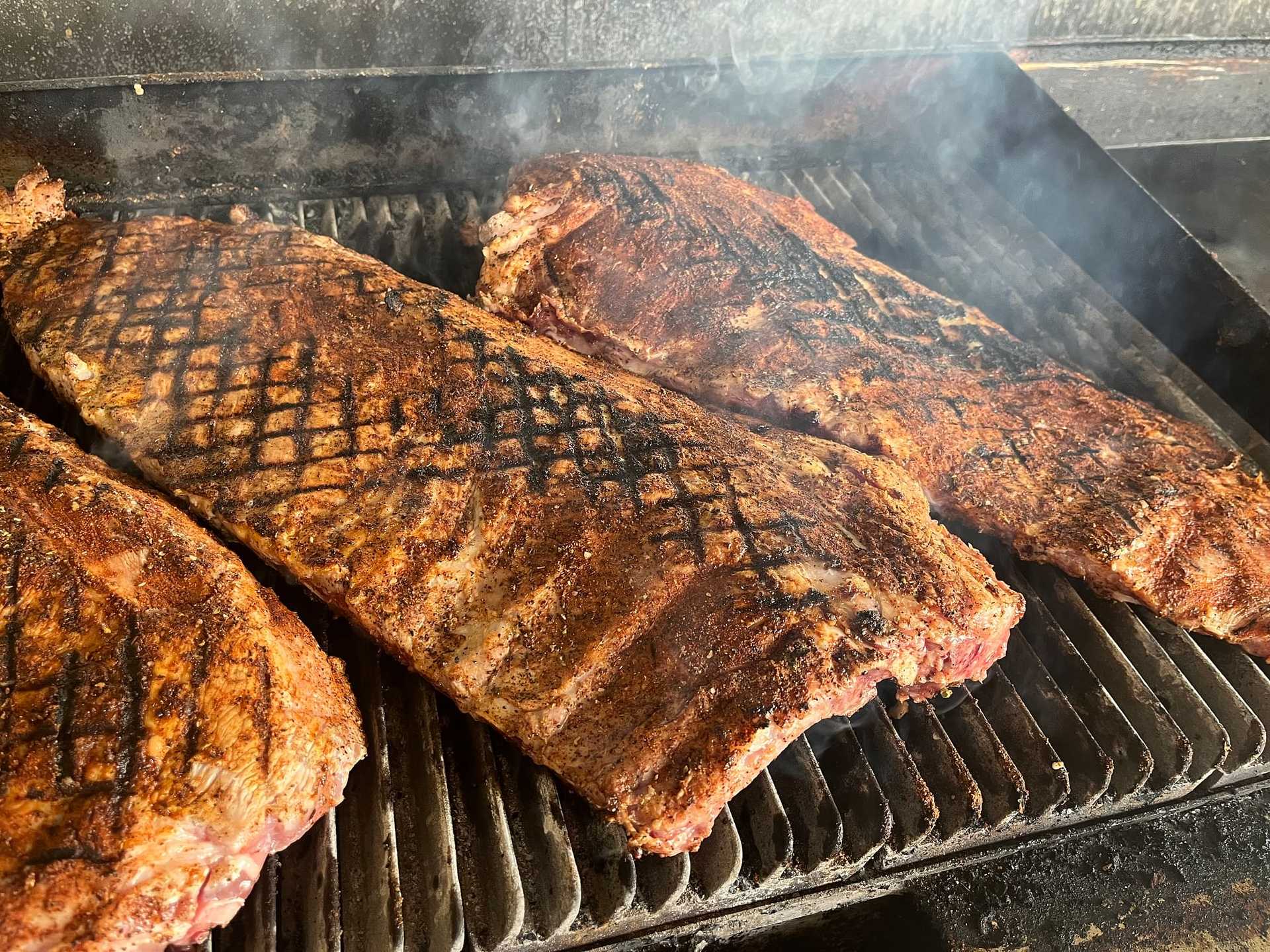 Ribs covered in seasoning being grilled with visible smoke.