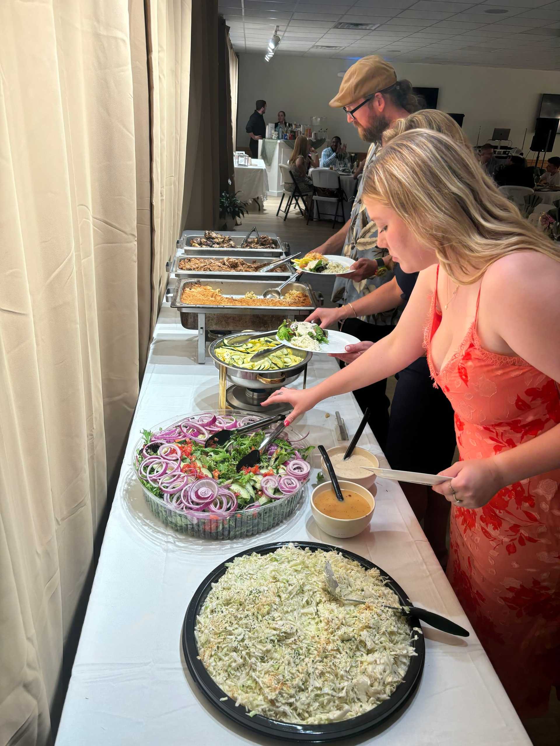 Guests serving themselves at a buffet with a variety of dishes including salad and rice pilaf.