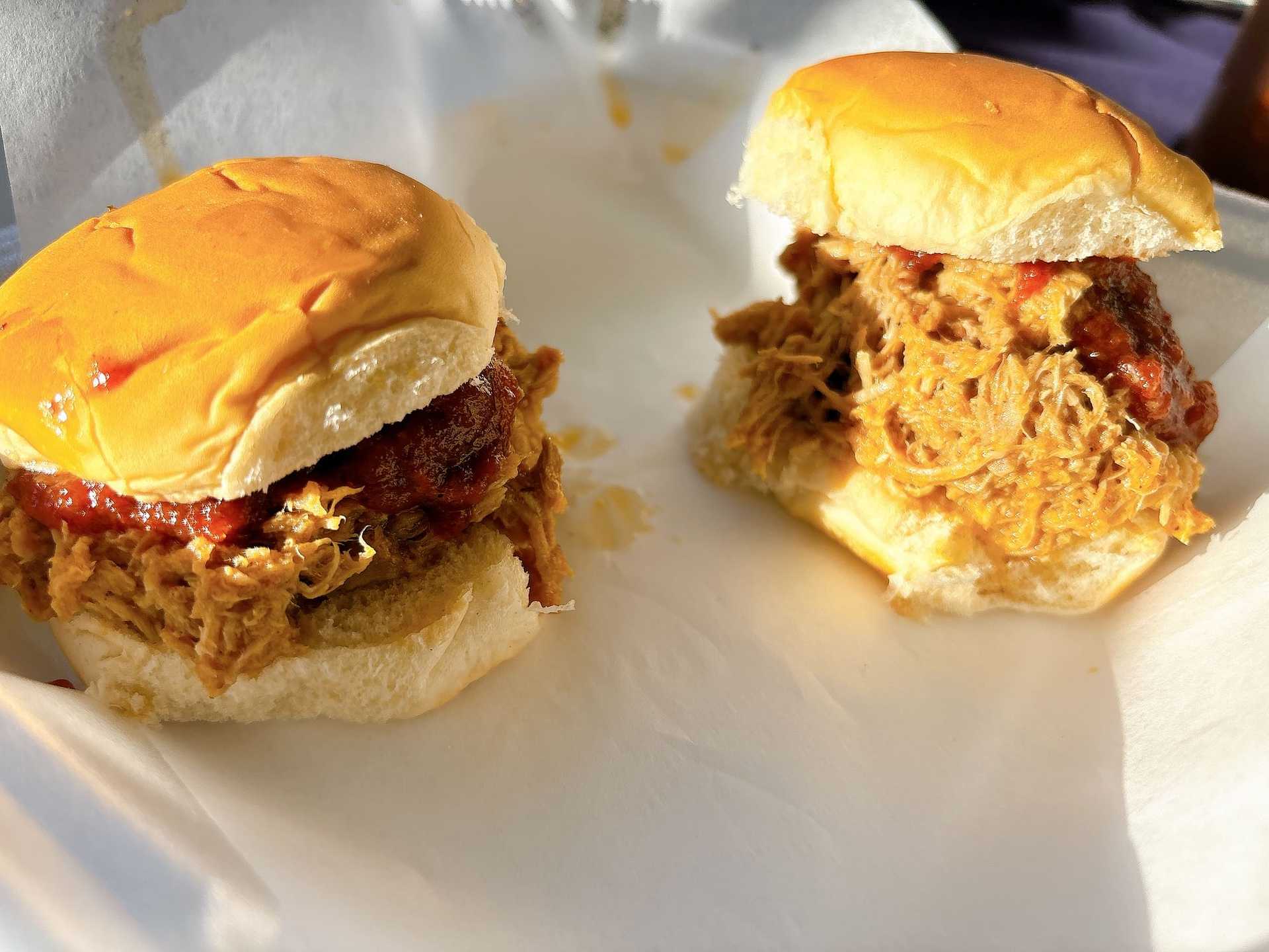 Two pulled pork sliders topped with barbecue sauce on a white plate.